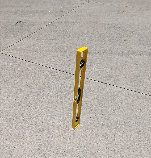 A level, sitting on a concrete footpath, showing a missing shadow. co eli fessler, wikicommons.